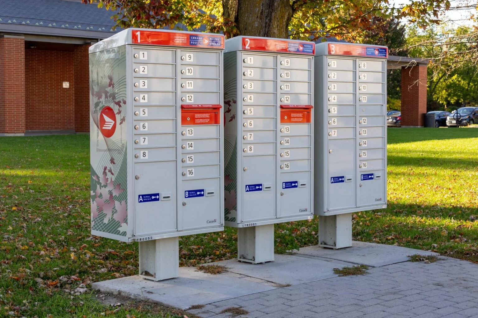 Canada Post Door-To-Door Delivery Cuts 2026 — Regina And Saskatoon Lose Home Mail Delivery Three Canada Post community mailboxes on a sunny street, central to the Canada Post Door-to-Door Delivery cuts coming to Regina and Saskatoon