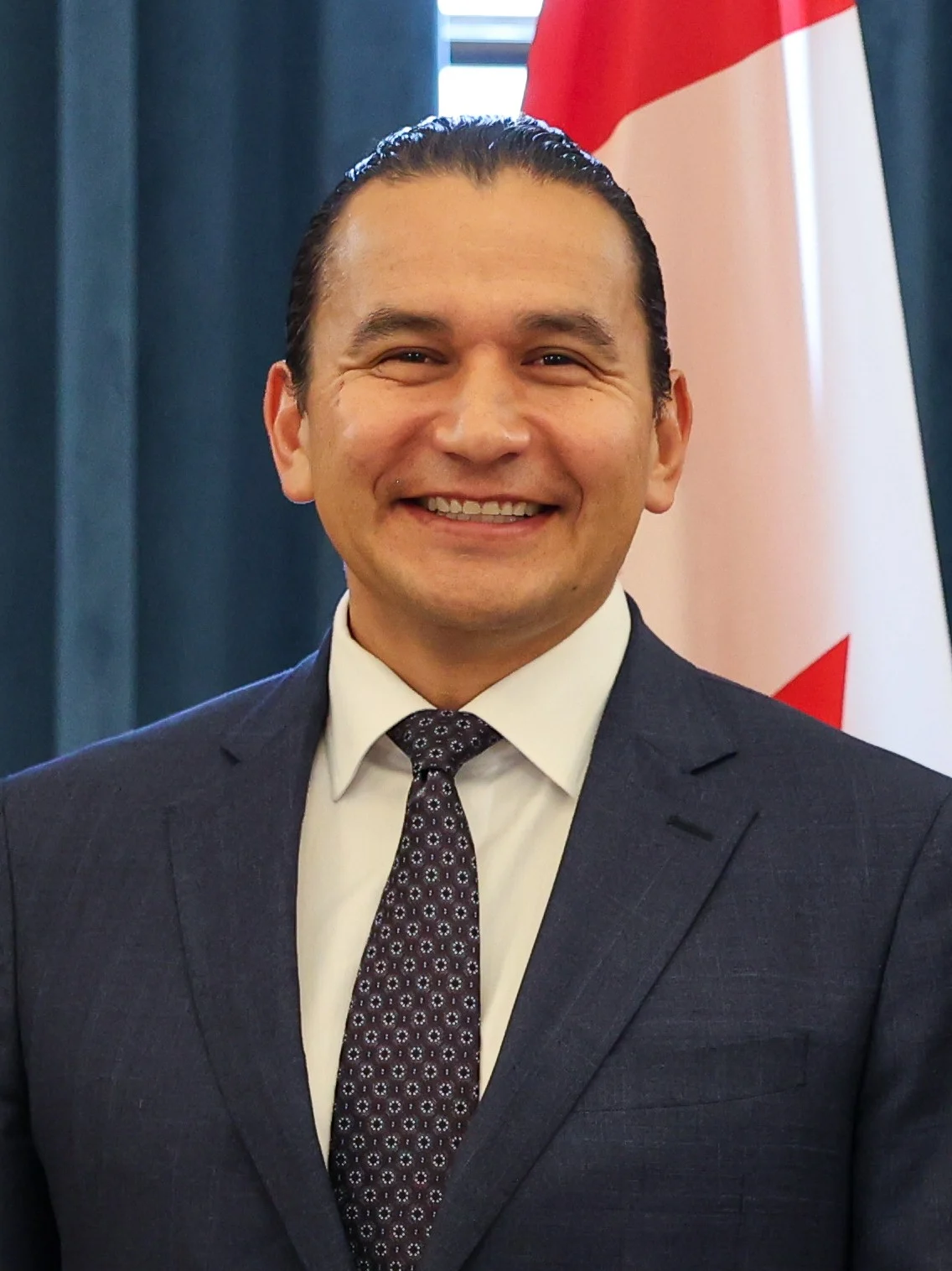 Manitoba Deficit 2026 — Province Cuts Deficit In Half To $832 Million And Eyes A Balanced Budget Next Year 2 Manitoba Deficit 2026: Manitoba Premier Wab Kinew smiling in a suit in front of the Canadian flag