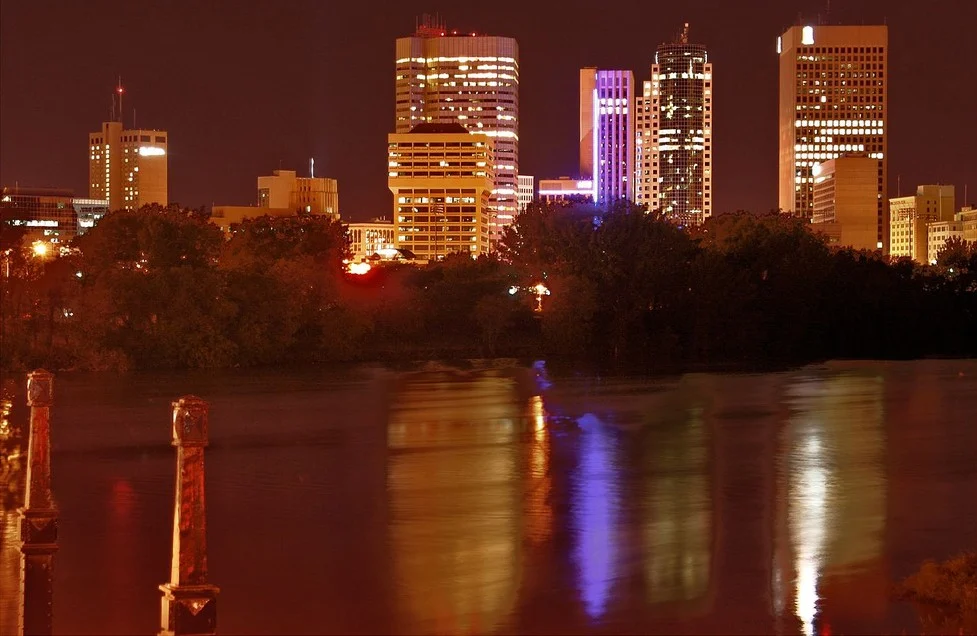Manitoba Deficit 2026 — Province Cuts Deficit In Half To $832 Million And Eyes A Balanced Budget Next Year 3 Manitoba Deficit 2026: Downtown Winnipeg skyline at night with lit office towers reflected on the river