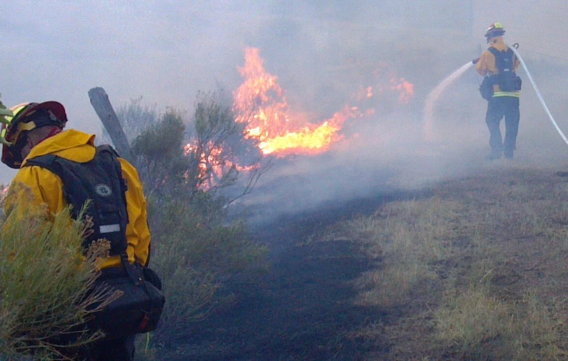 Newfoundland Wildfire Prevention Funding 2026 — Second Round Opens After Summer Blazes 1 Firefighters spraying water to slow the advance of a wildfire near a private home