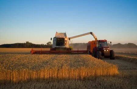 CLAAS Lexion combine harvester unloading in a wheat field; the AgWest Creditor Protection case puts the Manitoba equipment dealer up for sale