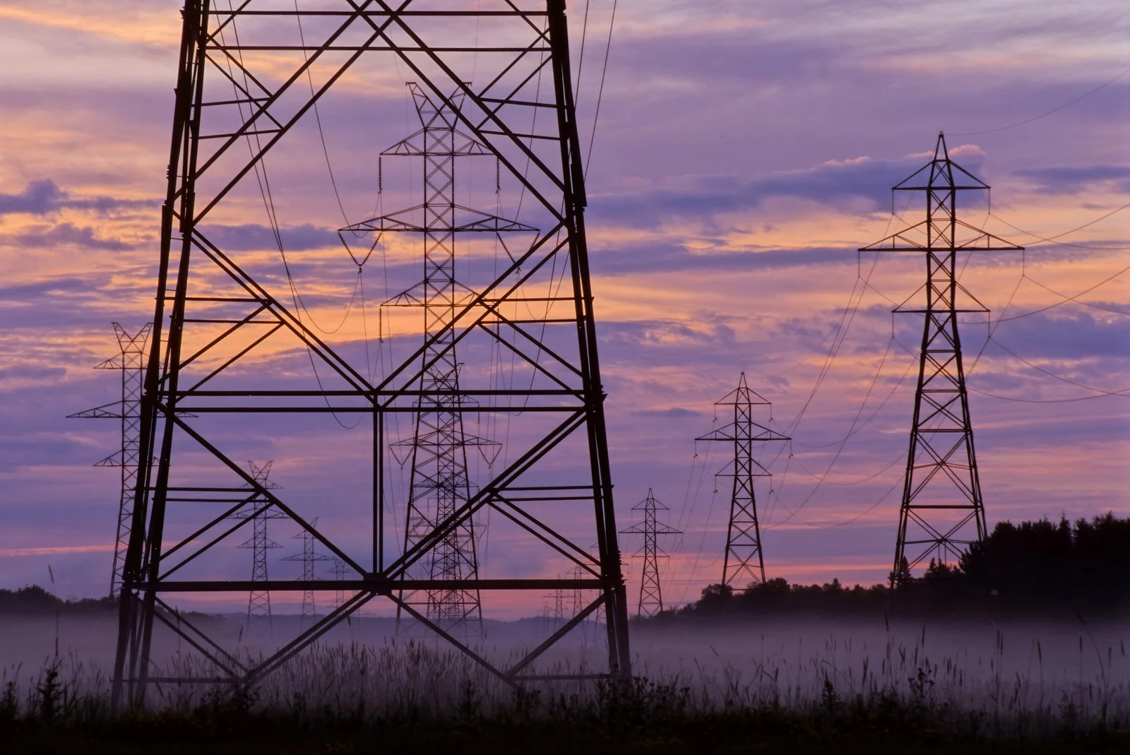 5 Wing Goose Bay Heating Plant 2026 — $187M To Move The Base Off Diesel 3 Electrical transmission towers at sunset (file photo), illustrating the grid connection that will power the 5 Wing Goose Bay Heating Plant