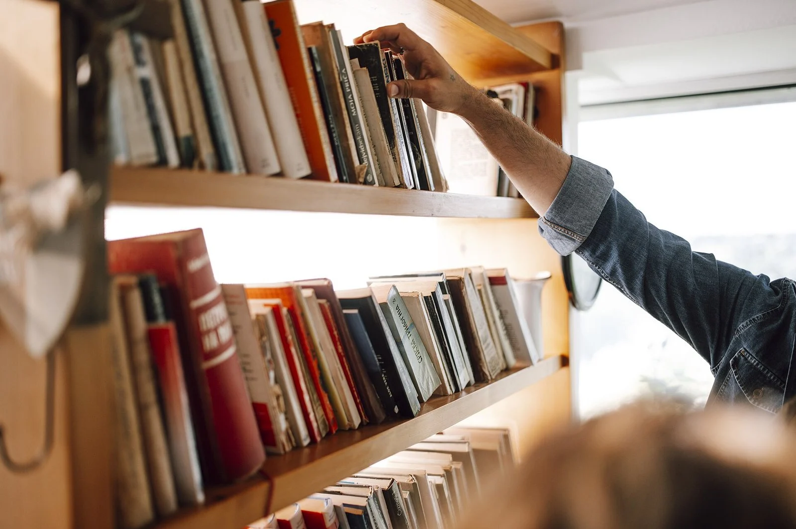 Manitoba Youth Centre Library Cut 2026 — Province Axes Volunteer Pop-Up Library 3 Person reaching for a book on a wooden shelf — Manitoba Youth Centre inmates lose librarian services (file photo)