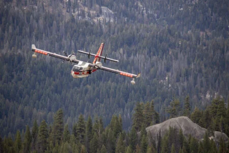2026 Wildfire Season Nova Scotia: 114 Fires, 1,521 Hectares, A Fraction Of Last Year’S Damage CL-415 water bomber flying over forest while fighting a wildfire, part of the aerial fleet credited in the 2026 wildfire season Nova Scotia response